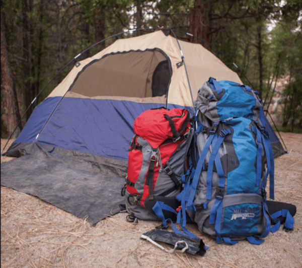 A tent and backpack set up in the woods.